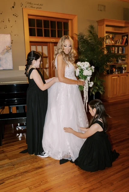 A bride in her gown with two flower girls adjusting the skirt