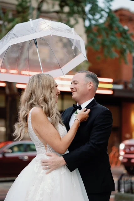 A bride with long waves under a clear umbrella, with the groom